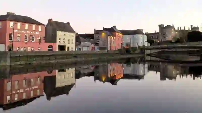 Kilkenny city at dusk with riverside houses, bridge and Kilkenny Castle reflected in the River Nore.