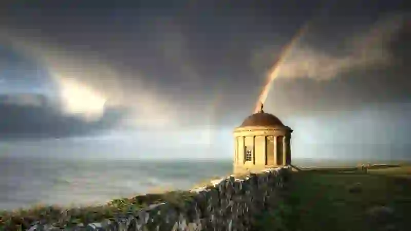 Mussenden Temple in County Londonderry framed by double rainbow above dramatic coastal cliffs.