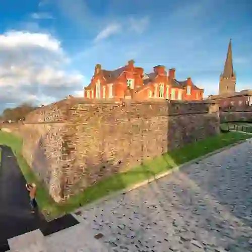 Historic Derry~Londonderry city walls beside red-brick buildings and cathedral spire.