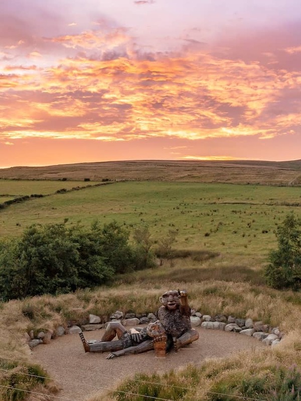 Wooden sculpture of giants in County Tyrone's Sperrin Mountains overlooking rolling countryside at sunset.