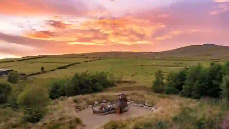 Wooden sculpture of giants in County Tyrone's Sperrin Mountains overlooking rolling countryside at sunset.