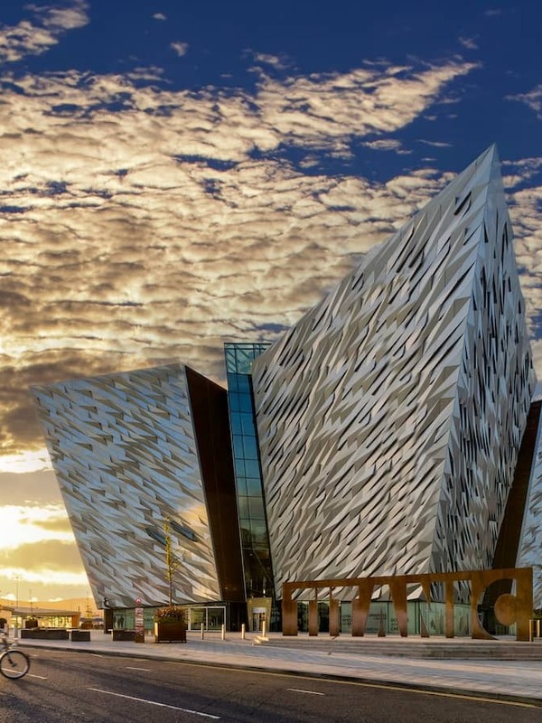 Titanic Belfast at sunset, with cyclists passing along the waterfront in Belfast’s Titanic Quarter.