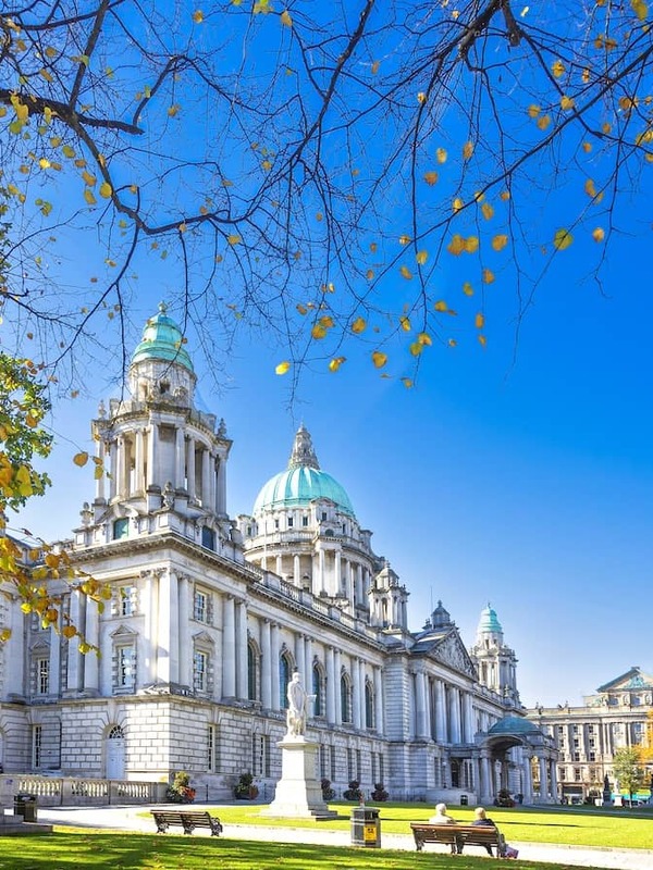 Belfast City Hall framed by autumn leaves, its green domes rising above the lawns and statues.