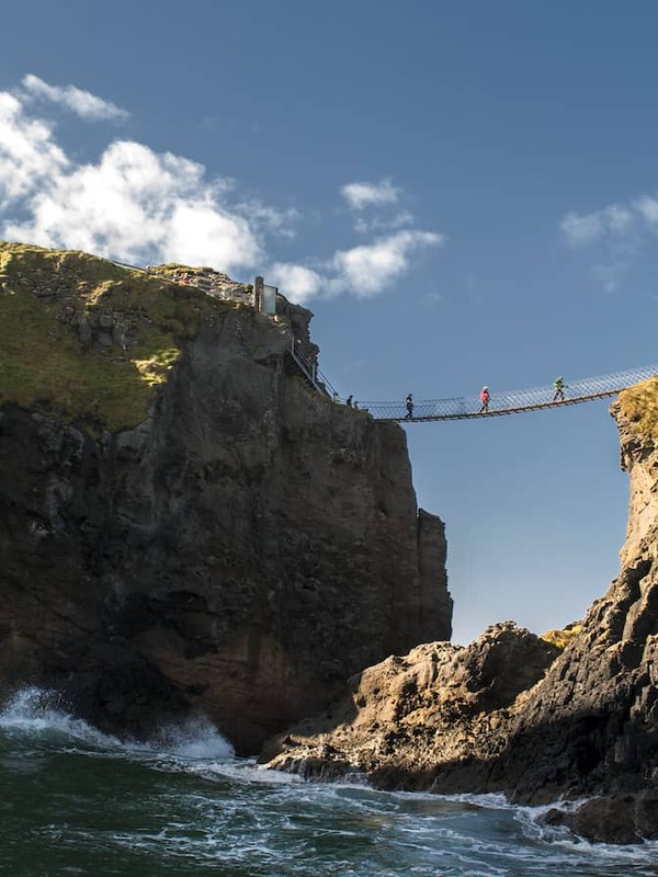 Visitors crossing the Carrick-a-Rede Rope Bridge between rugged sea cliffs on the Antrim Coast.
