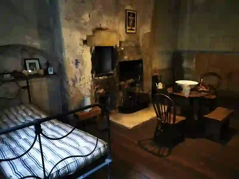Interior of a historic tenement room with iron bed, wooden furniture, and an old fireplace in Dublin museum.