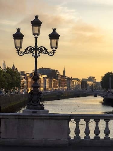 View of O'Connell Bridge and city skyline lit by golden evening light over the River Liffey.