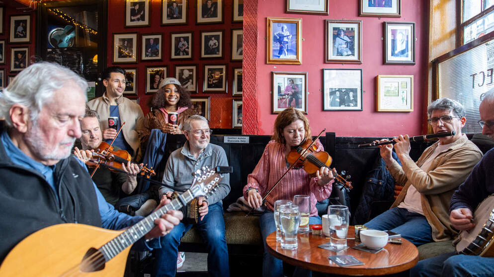 Three traditional musicians playing fiddle, flute, and guitar in a moody pub setting, representing top trad music pubs in Dublin.
