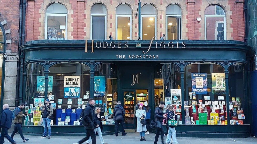 Busy entrance of Hodges Figgis in Dublin with readers browsing books; sign reads 'A guide to Dublin’s best bookshops.'