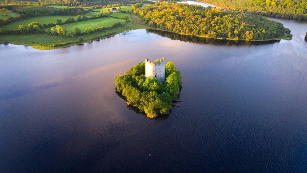Aerial view of Cloughoughter Castle on a wooded island in Lough Oughter, County Cavan, surrounded by calm water.