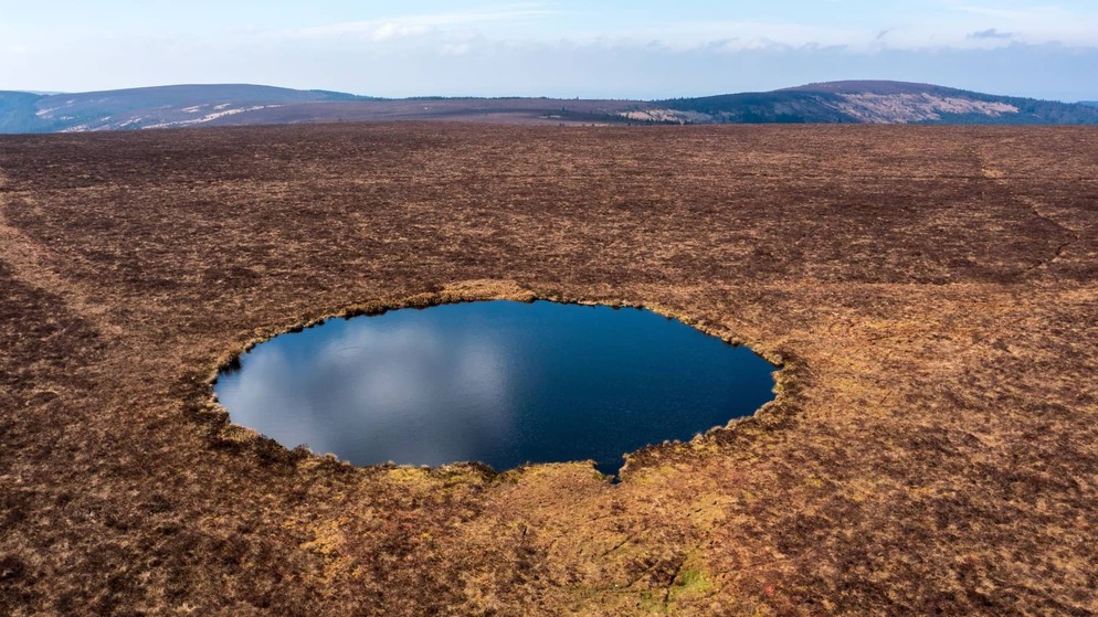 Aerial view of Clear Lake in the Slieve Bloom Mountains, County Offaly, a small circular lake surrounded by open peatland under a blue sky.