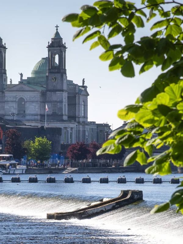 View of Athlone on the River Shannon, County Westmeath, with St Peter and Paul’s Church framed by green leaves on a summer day.