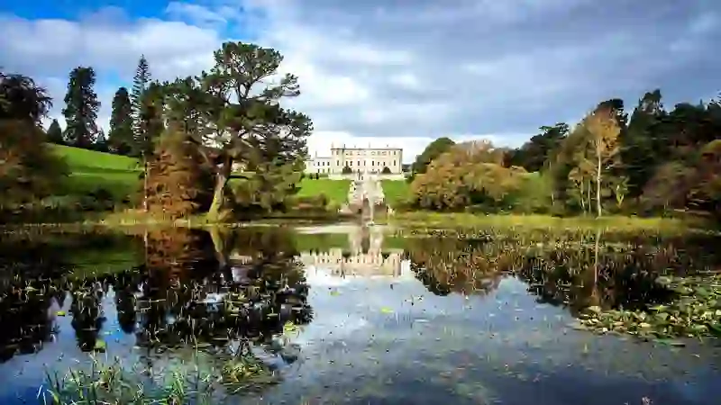 Powerscourt House in County Wicklow overlooking landscaped gardens and lake, framed by mature trees and rolling lawns.