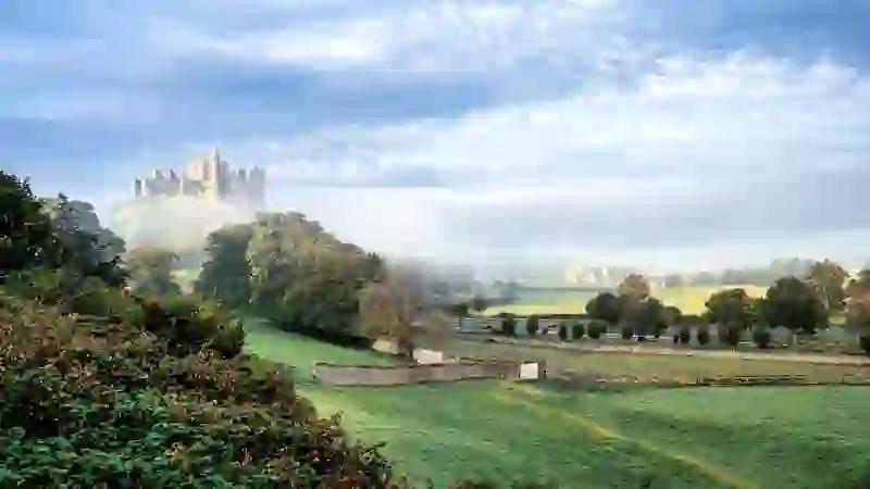 Rock of Cashel rising above green farmland of County Tipperary, with medieval stone buildings framed by misty morning light.