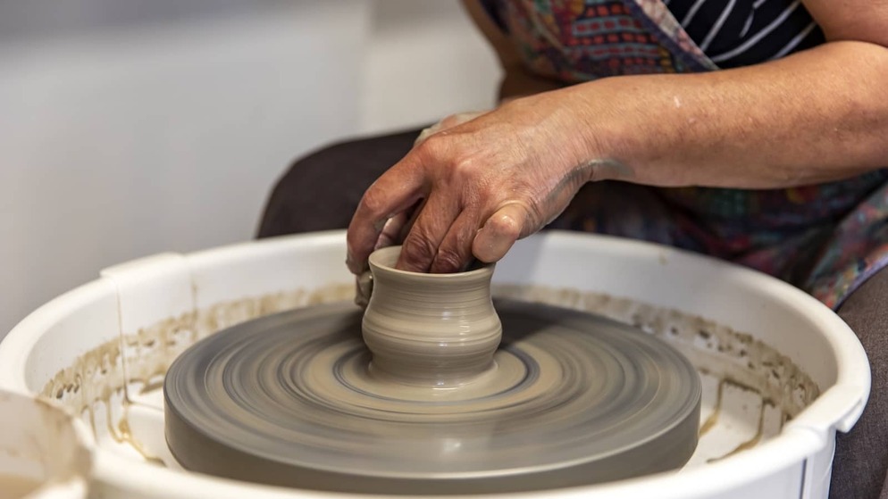 Hands shaping a clay pot on a spinning pottery wheel during a ceramics workshop at Mount Brandon Pottery School, County Kilkenny.