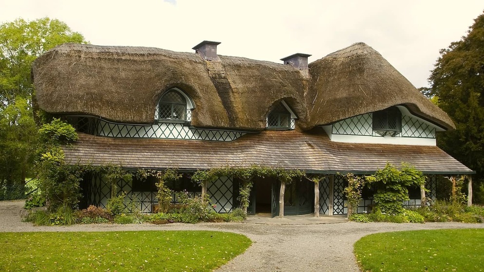 Traditional thatched Swiss Cottage in County Tipperary with timber detailing, surrounded by gardens and trees.
