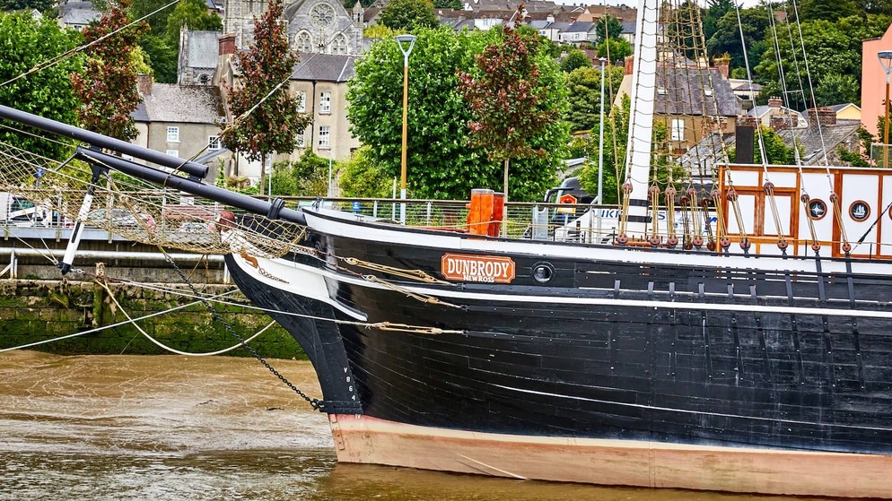 Dunbrody Famine Ship moored on the River Barrow in New Ross, County Wexford, with historic buildings behind.