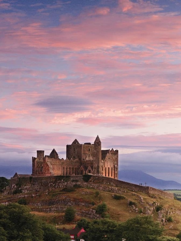 Rock of Cashel in County Tipperary, silhouetted on a hilltop above green countryside under a vivid pink and blue sunset sky.