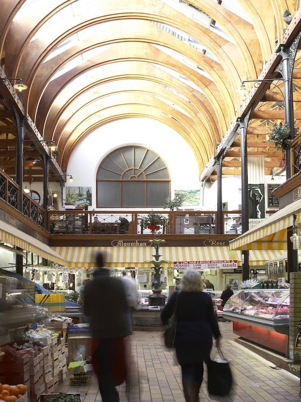 Interior of the English Market in Cork, with fresh produce stalls, deli counters and shoppers under a vaulted ceiling.