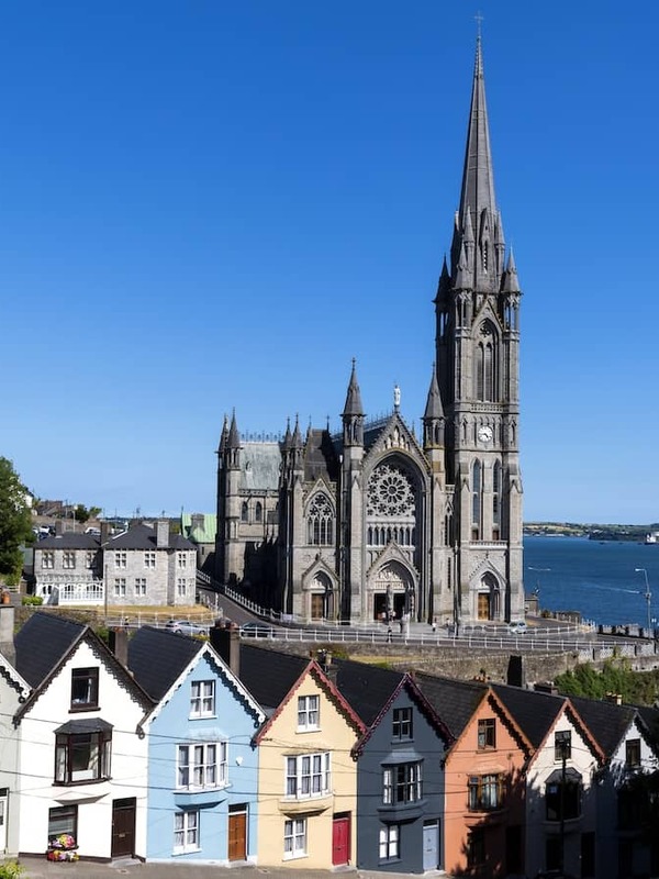 St Colman’s Cathedral towering above colourful houses in Cobh, overlooking Cork Harbour on a sunny day.