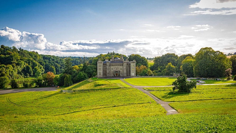 Slane Castle in County Meath, set on a grassy hillside with trees and countryside under a bright sky.