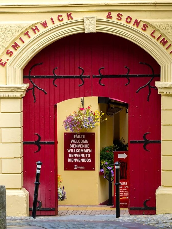 Red arched entrance to the Smithwick’s Experience in Kilkenny, with hanging flowers and a welcome sign inside.