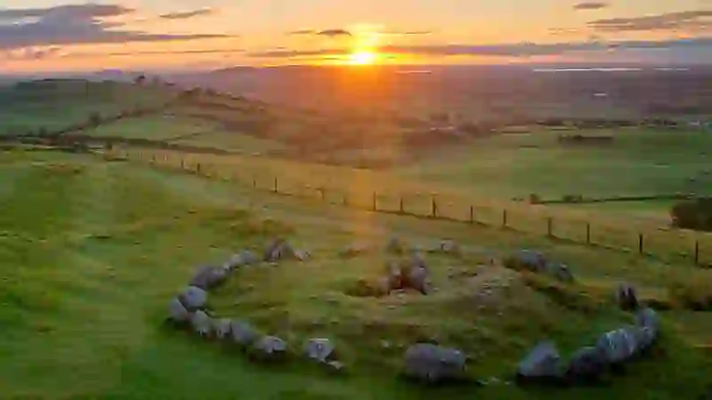 Sunset over the Loughcrew Cairns in County Meath, with a stone circle on grassy hills overlooking patchwork farmland.