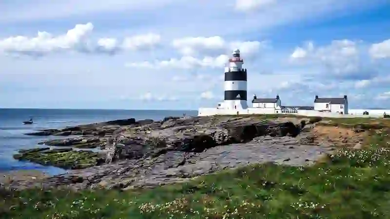 Hook Head Lighthouse on the County Wexford coast, standing above rocky cliffs beside white cottages and the sea.