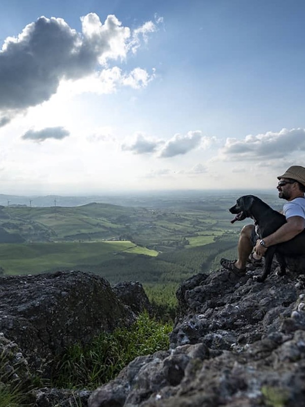 Man sitting with his dog on a rocky viewpoint, overlooking the Devil’s Bit mountains and green countryside in County Tipperary.