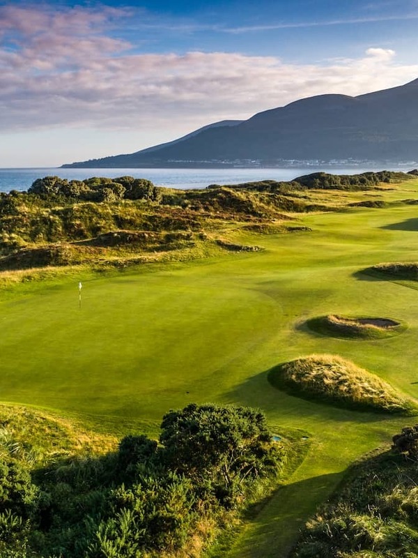 Lush fairways of Royal County Down golf course with sea views and the Mourne Mountains in the distance.