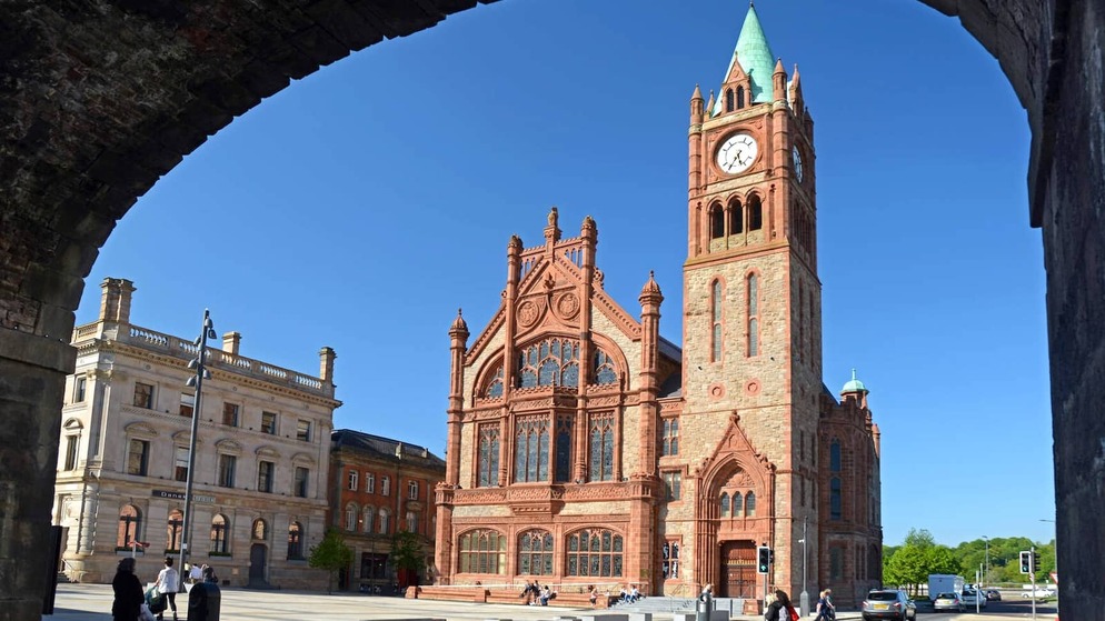 Neo-Gothic red-brick Guildhall with clock tower framed by a stone arch in Derry~Londonderry’s historic city centre.