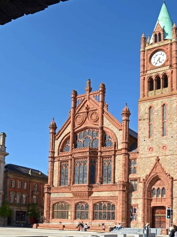 Neo-Gothic red-brick Guildhall with clock tower framed by a stone arch in Derry~Londonderry’s historic city centre.