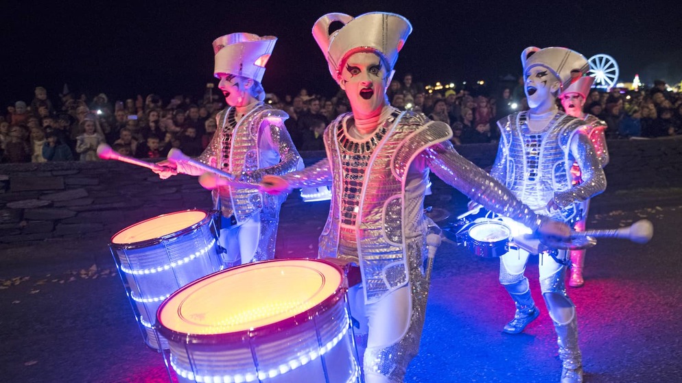 Street drummers in silver costumes entertaining crowds at Derry Halloween night parade.