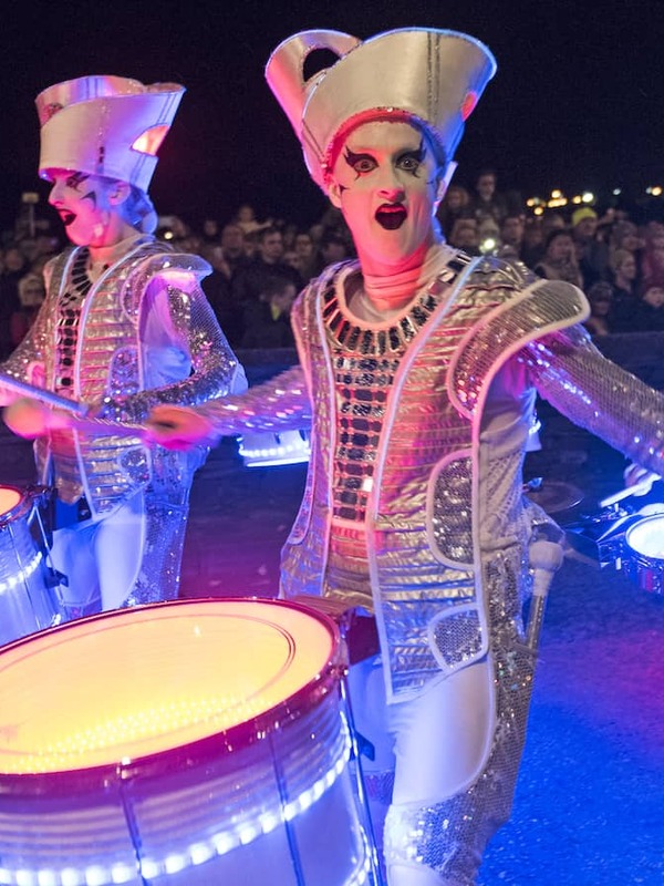 Street drummers in silver costumes entertaining crowds at Derry Halloween night parade.