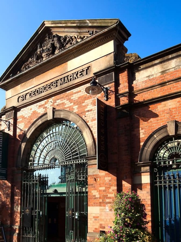 Red-brick Victorian facade of St George’s Market with arched gates and a café terrace in Belfast.