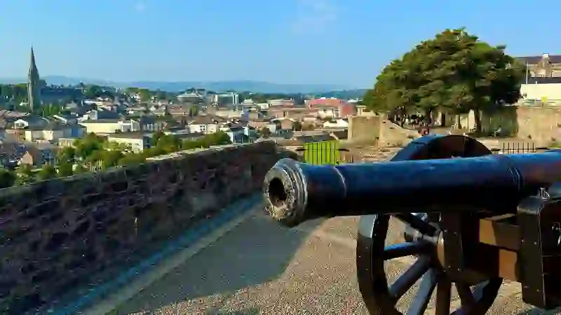 Historic cannon on Derry~Londonderry’s city walls overlooking rooftops and church spires under a blue sky.
