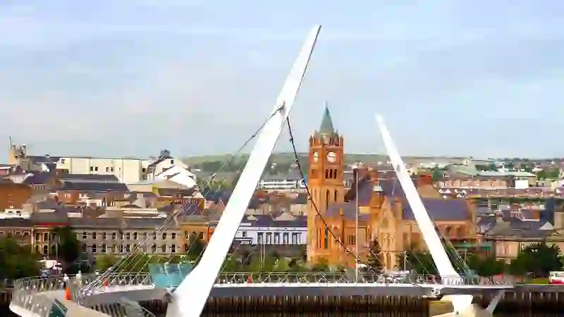 The Peace Bridge curving over the River Foyle with Derry~Londonderry’s Guildhall in the background, Northern Ireland.