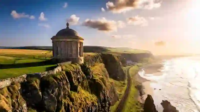 Mussenden Temple overlooking cliffside railway and coast at sunset in County Londonderry, Northern Ireland.