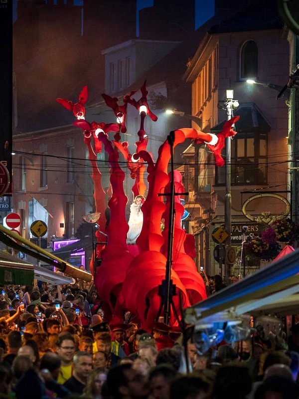 Vibrant red creature-themed float moves through a bustling, lantern-lit street at the Galway International Arts Festival.
