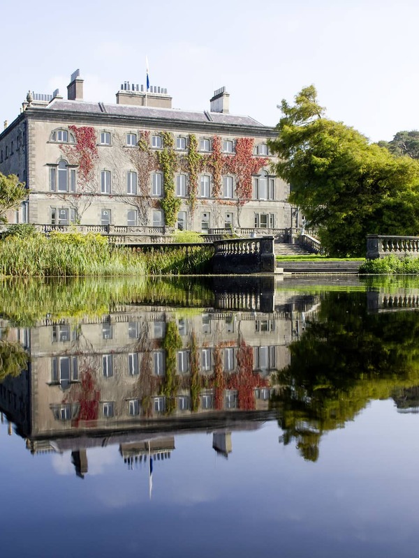 Elegant Westport House in County Mayo reflected in a still lake, surrounded by lush gardens and mature trees.