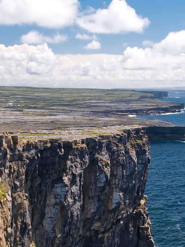 Visitors explore rocky cliffs beside the ancient stone fort of Dún Aonghasa on Galway’s Aran Islands.