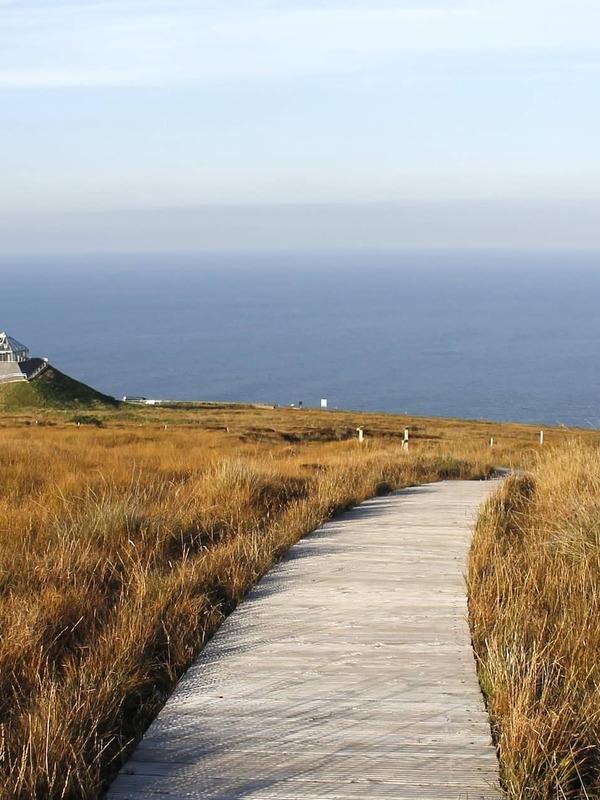 Wooden boardwalk leading through golden moorland to the pyramid-shaped Céide Fields visitor centre overlooking the Atlantic.