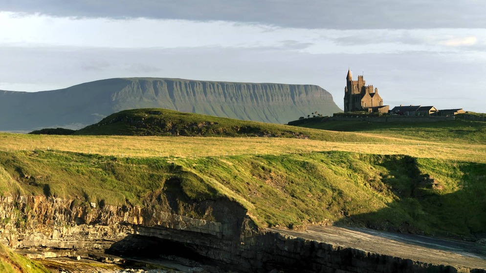 Classiebawn Castle perched on green headland with Ben Bulben mountain in the background, County Sligo.