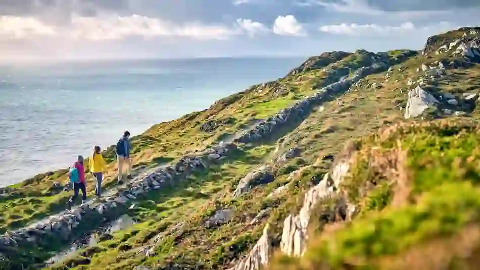 Group of hikers walk a rugged coastal trail on the Sheep’s Head Way in County Cork, overlooking the Atlantic Ocean.
