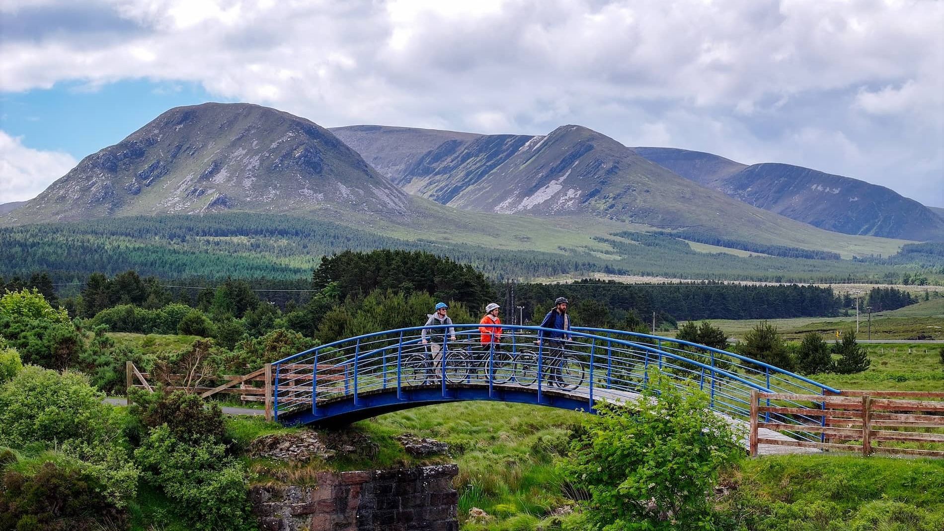 Cyclists cross a bridge on the Great Western Greenway in County Mayo with Nephin Beg mountains in the background.