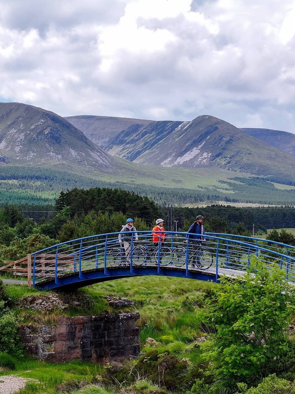 Cyclists cross a bridge on the Great Western Greenway in County Mayo with Nephin Beg mountains in the background.