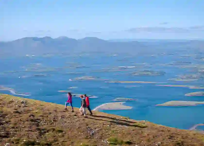 Three hikers walk above Clew Bay in County Mayo with views of its drumlin islands and distant mountains.