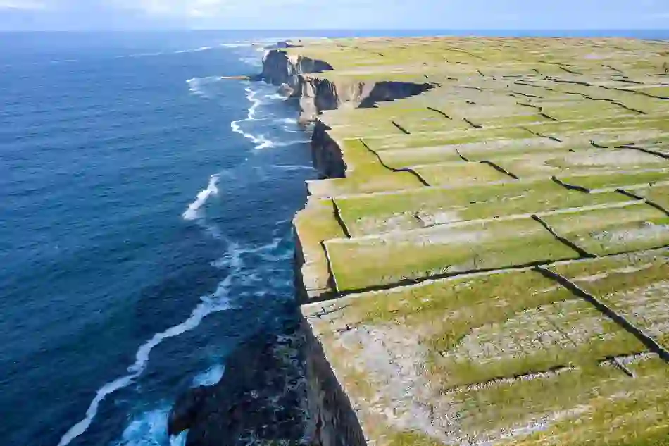 Stone-walled fields stretch to steep sea cliffs on Inis Mór, one of the Aran Islands in County Galway, with deep blue ocean below.