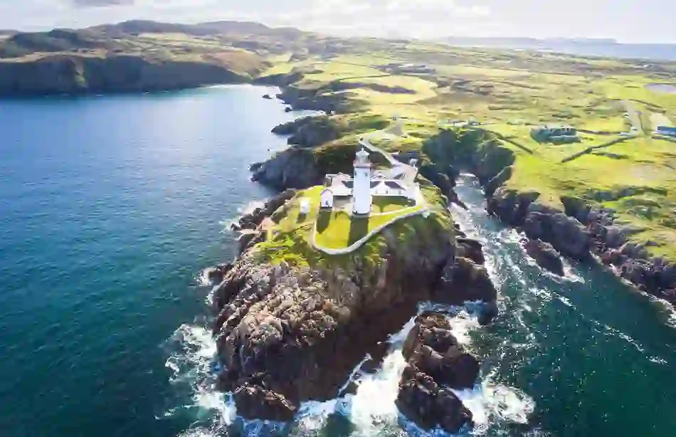 White lighthouse on a rocky Donegal headland, surrounded by dramatic coastline and open Atlantic sea.