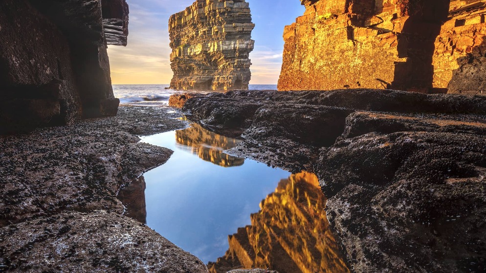 Sea stack at Downpatrick Head reflecting in a tidal pool beneath rugged cliffs on the Mayo coast at sunset.