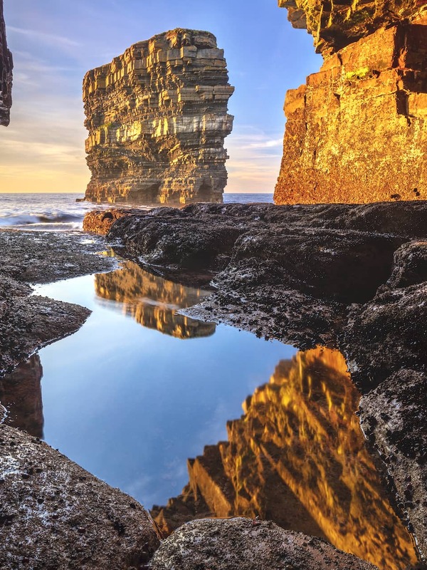 Sea stack at Downpatrick Head reflecting in a tidal pool beneath rugged cliffs on the Mayo coast at sunset.